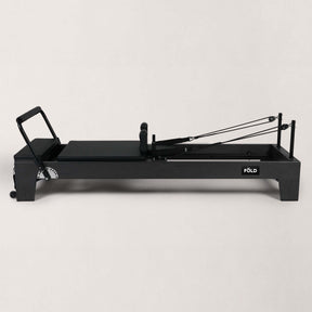FOLD STUDIO Reformer machine with black vegan upholstery and hardwood frame, designed for home or commercial use.