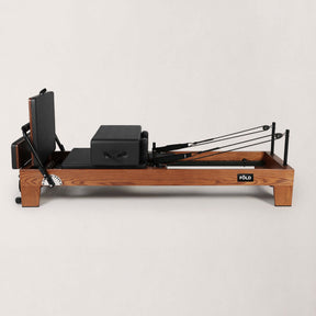 FOLD STUDIO Reformer side view showcasing premium hardwood frame and black upholstery.