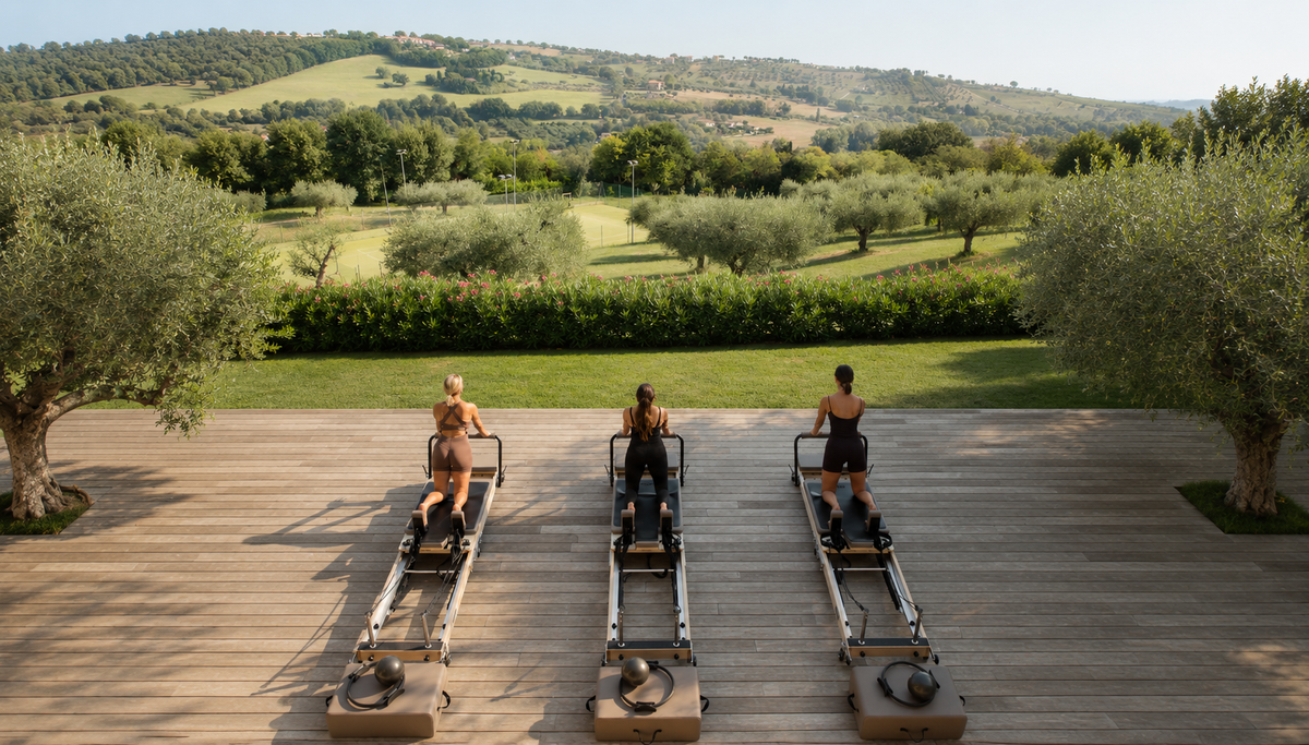 Three women practicing Pilates outdoors on reformers with a scenic green landscape in the background.