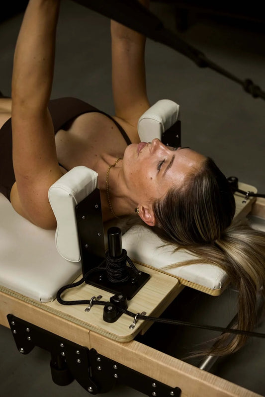 What happens in reformer pilates class? A woman practicing on a Reformer Pilates bed.