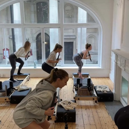 Image of students in a Pilates studio, focusing on strength training while using a reformer, highlighting Choosing the Right Booking Platform for Your Pilates Studio.