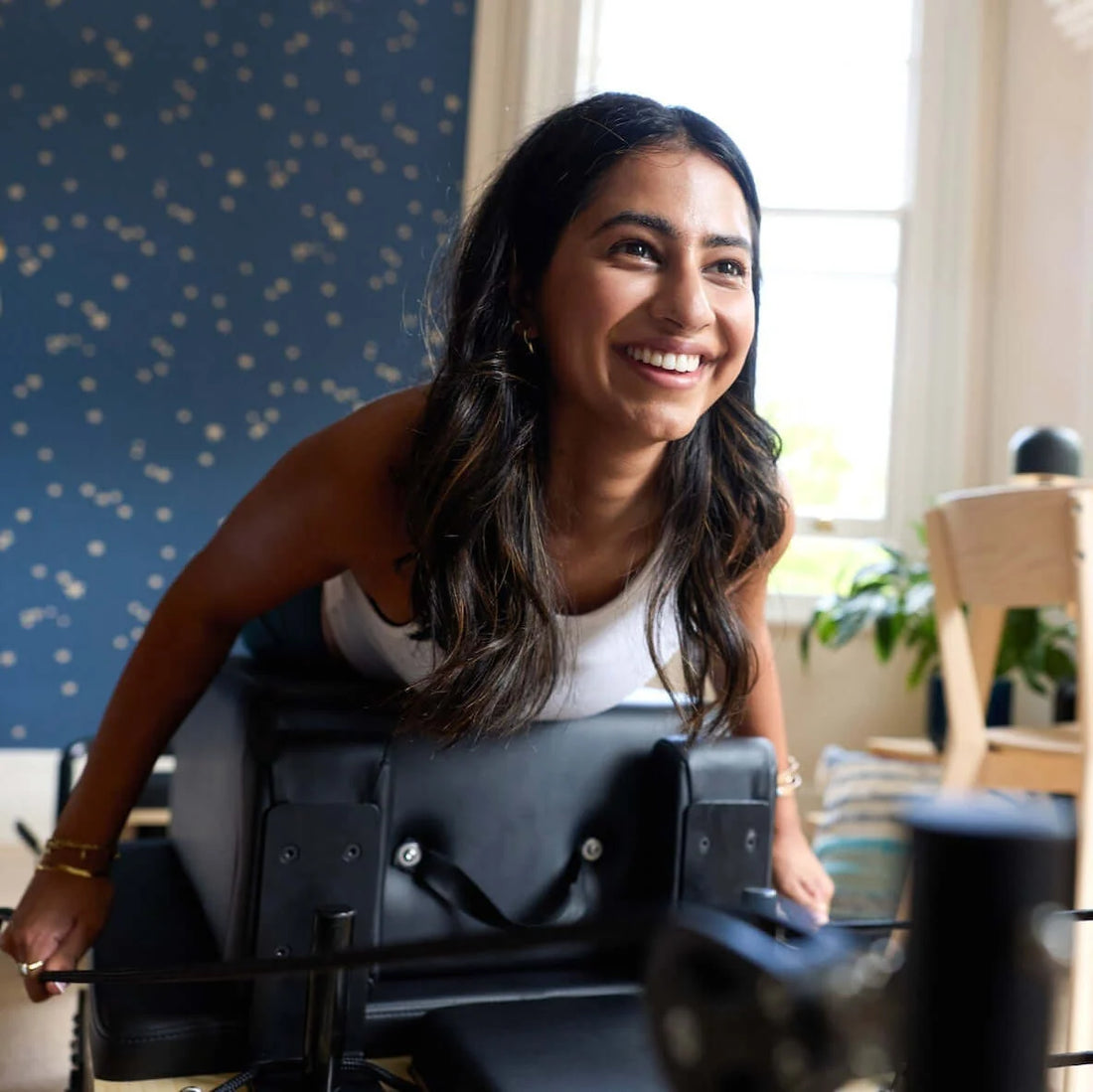 Smiling woman exercising on a reformer for Home Reformer Pilates: The Easy Way to Exercise at Home.
