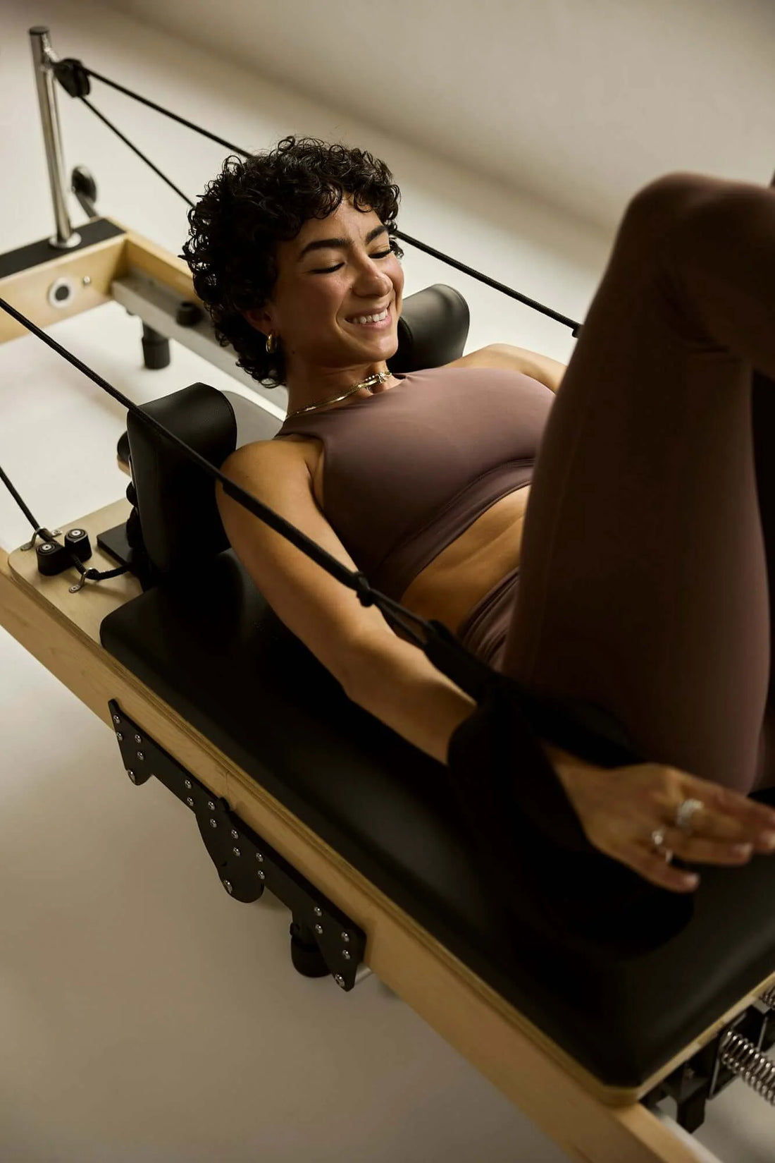Ultimate Pilates Reformer Workouts for Stronger Core: woman smiling while doing exercises on a Pilates reformer machine.