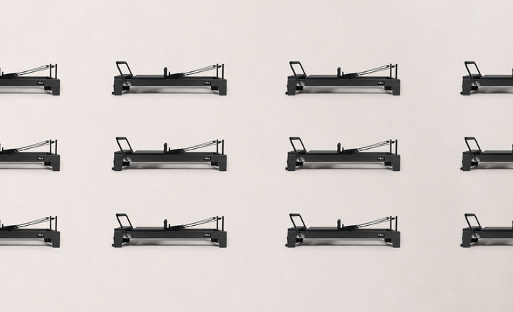 Eight black fitness reformer machines arranged neatly on a pale background.