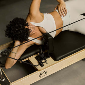 Women lying outstretched on a black FOLD Reformer bed with leg in a strap