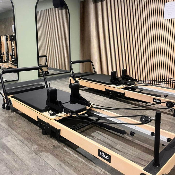 Two pilates reformers in a sleek studio with wooden accents, ready for workout sessions at the FÖLD gym.