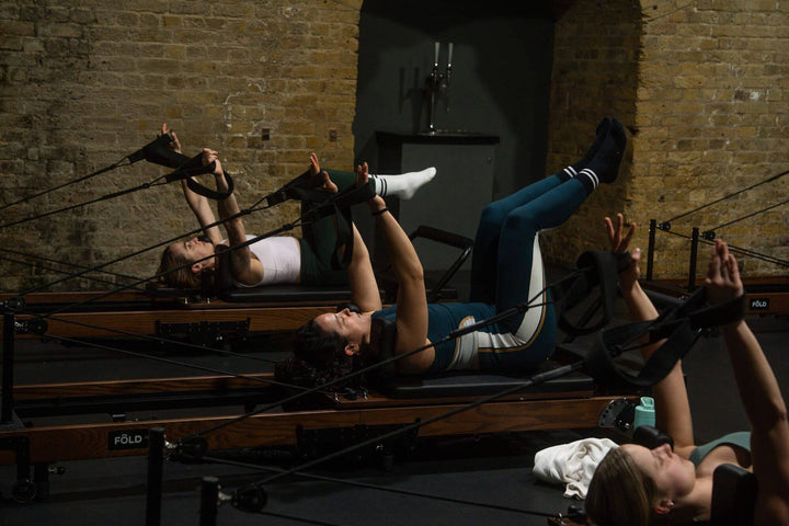 Group of women engaged in a Pilates reformer class, focusing on stretching and core strength.