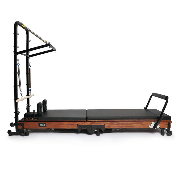 FOLD's pilates tower reformer machine in black and red oak on a white background