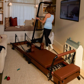 Woman using a Pilates reformer machine in a home setting.