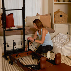 Woman using a Pilates reformer machine in a home setting.