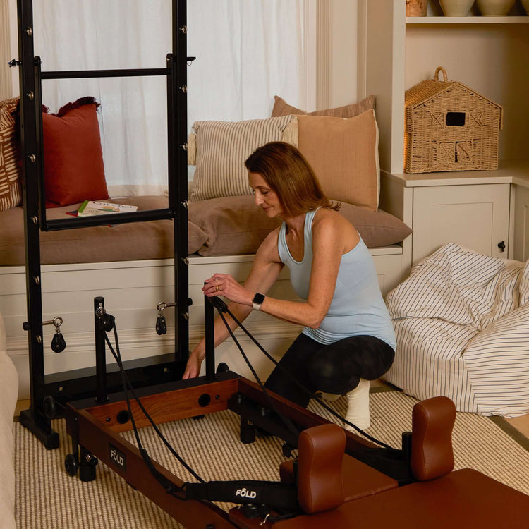 Woman using a Pilates reformer machine in a home setting.