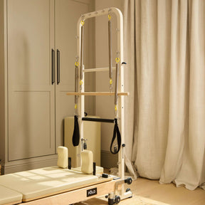 Tower pilates reformer machine in a home setting with curtains and cabinets in the background.
