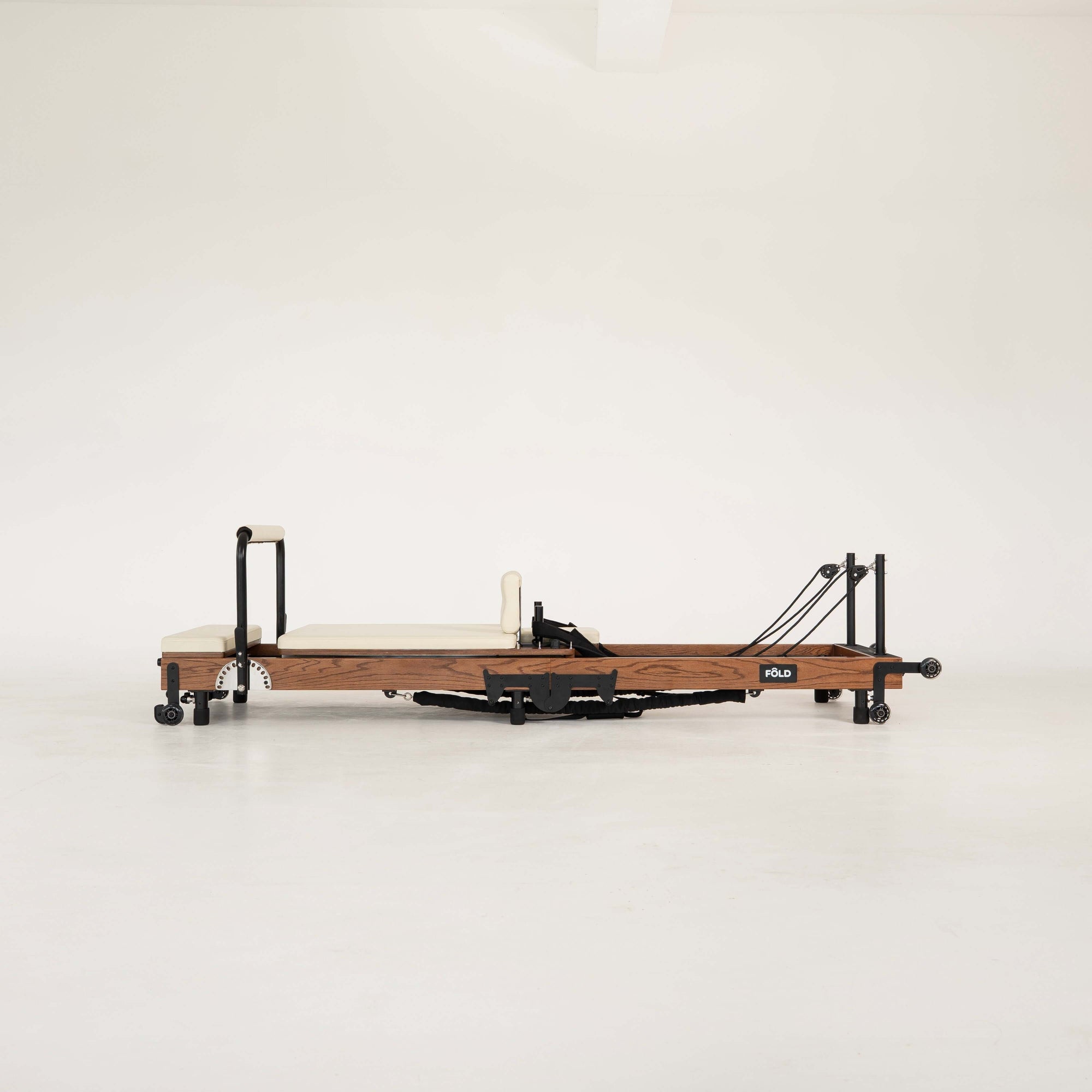 Dark Wooden Pilates reformer with beige/vanilla upholstery on a white background