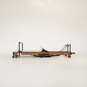 Dark Wooden Pilates reformer with beige/vanilla upholstery on a white background