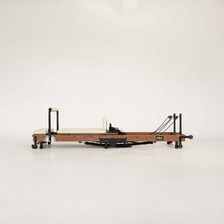 Dark Wooden Pilates reformer with beige/vanilla upholstery on a white background