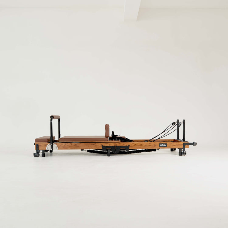 Dark wooden Pilates reformer with brown/chocolate upholstery on a white background