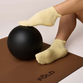 Pilates Low Rise Grip Socks - Butter Yellow worn during a workout, resting on a black ball on a brown mat.