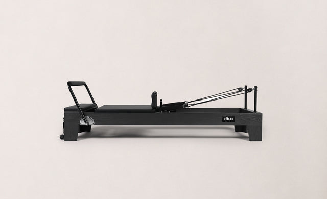 Black Pilates reformer fitness equipment on a light background, designed for strength and flexibility training.