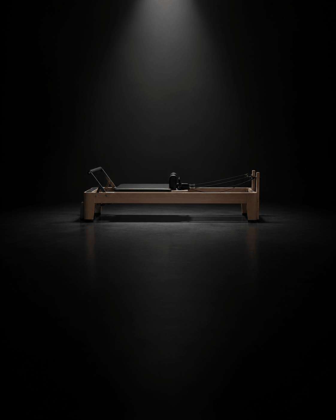 Wooden Pilates reformer machine illuminated against a dark background, showcasing its sleek design and features.