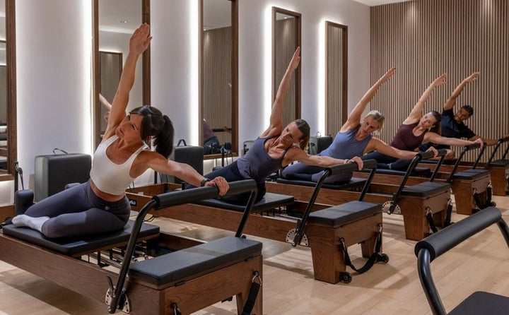 Women practicing Pilates on reformers in a modern studio, focusing on flexibility and strength training.
