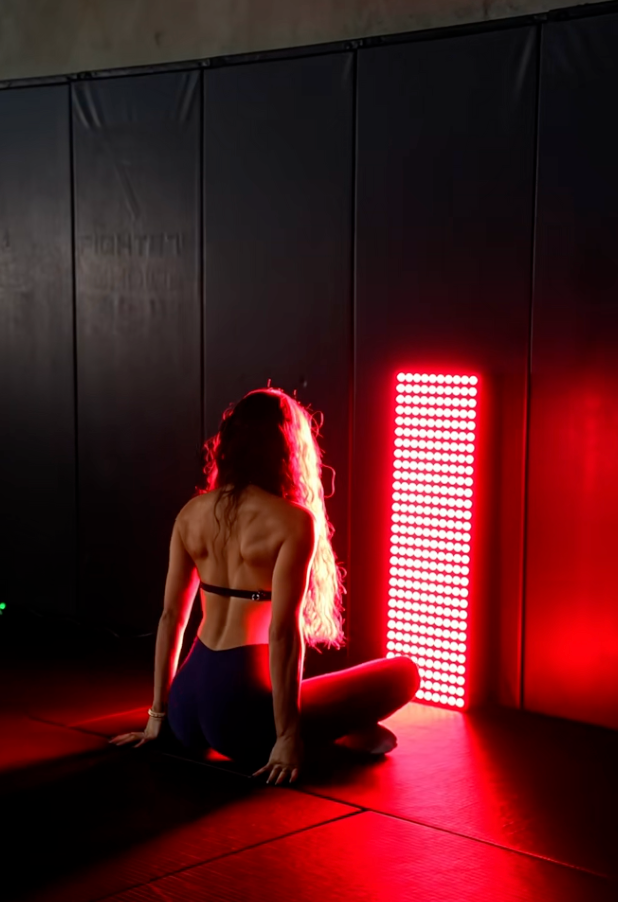 Person sitting on the floor with a red light panel behind them in a dark room.