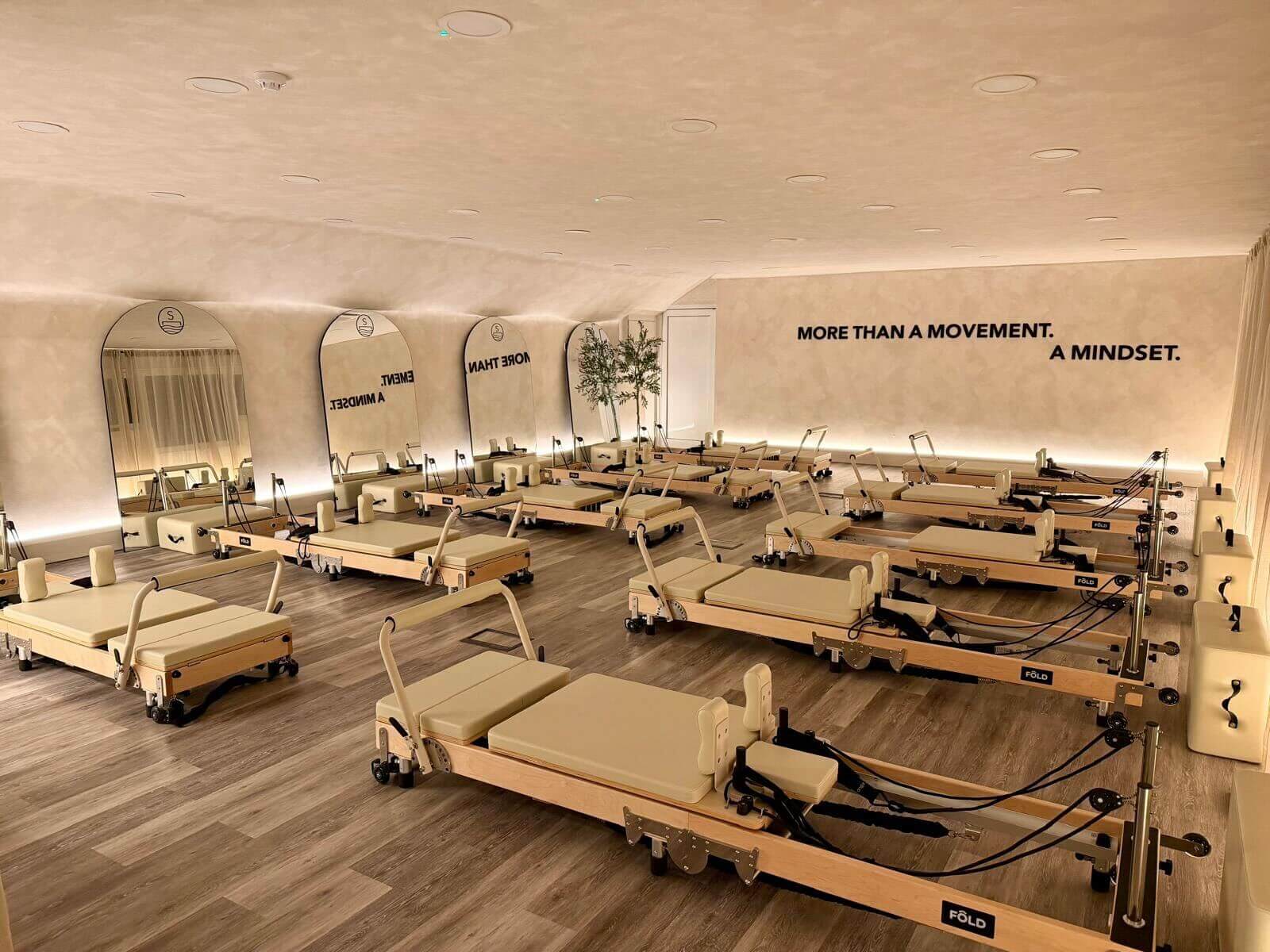 Pilates reformers in a studio with mirrors and motivational wall text.